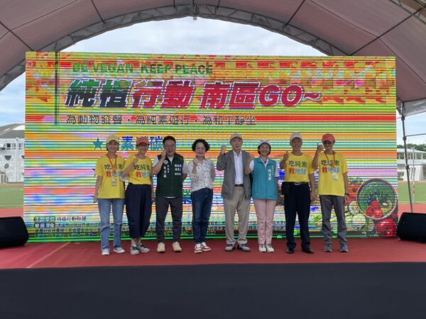 主辦單位、貴賓與參與民眾一同登台合影，手持標語高喊口號，為「純素減碳、友善動物、推動永續農業」畫下圓滿句點，象徵共同守護地球、推動純素立法的決心。圖/主辦單位提供